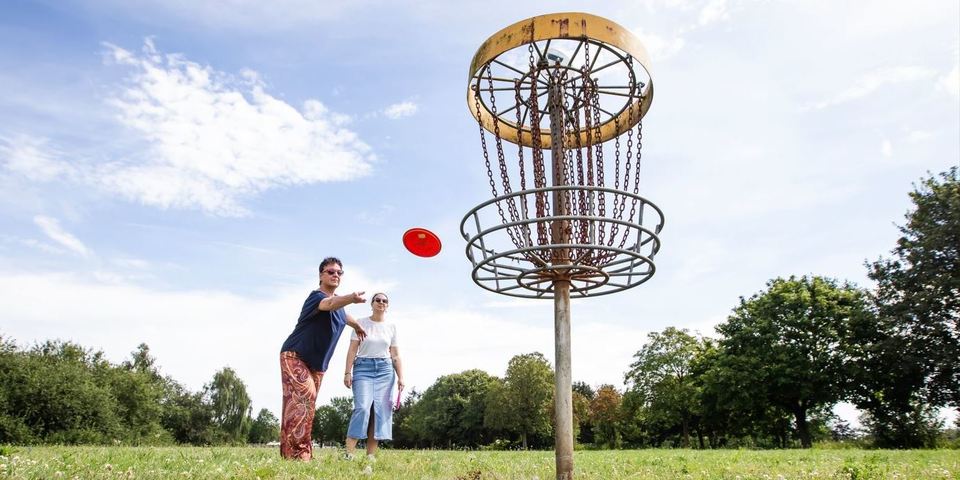 Twee volwassenen spelen disc golf in de groene omgeving van Fort 3